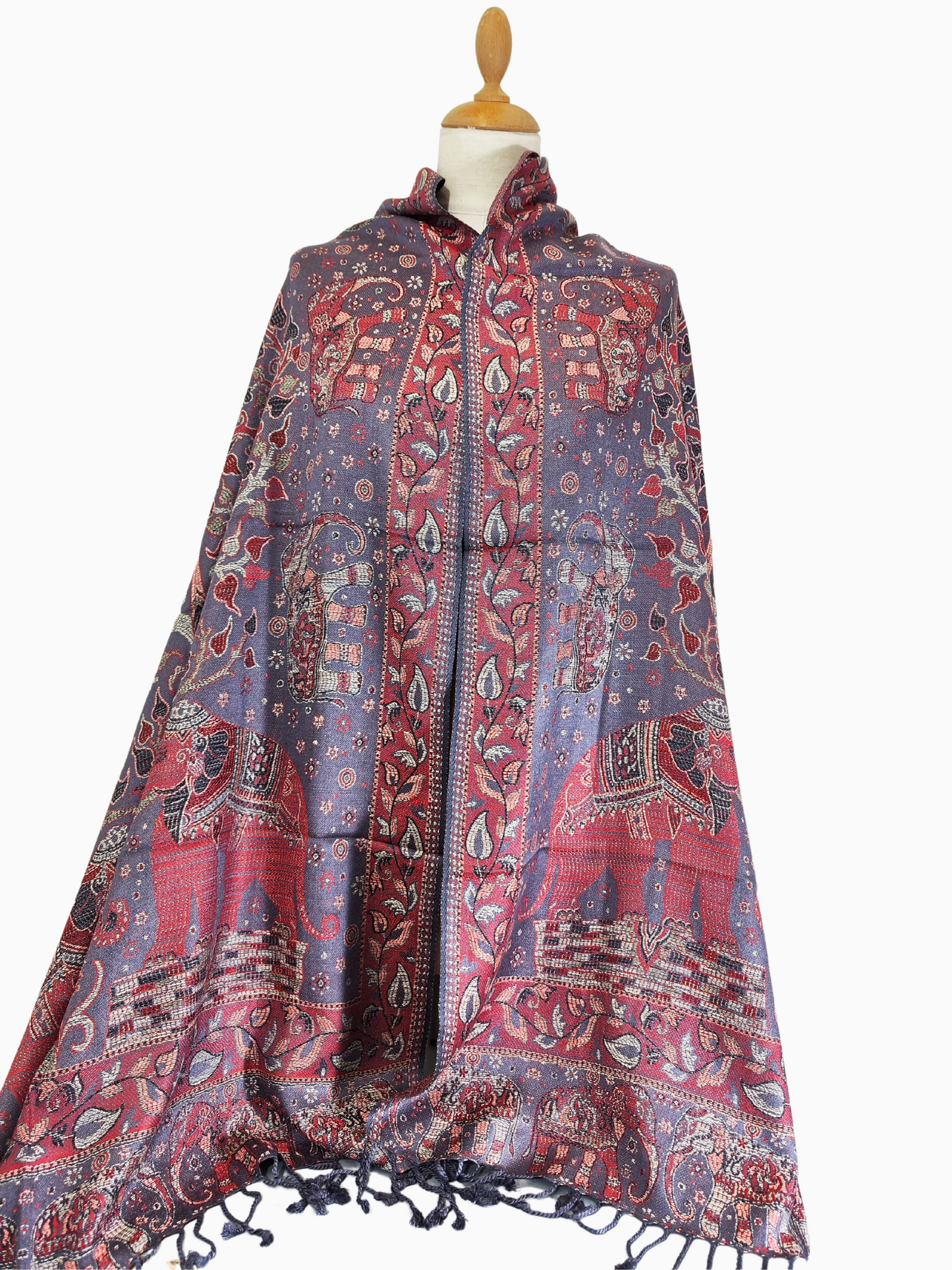 Châle en pashmina au tissage complexe sur fond violet, orné de motifs éléphants et floraux rouges, dorés et bleus, et de pampilles.
Luxueux châle en pashmina avec un mélange captivant de violet, de rouge, d'or et de bleu, orné d'élégants motifs d'éléphants et de fleurs et terminé par des glands.
