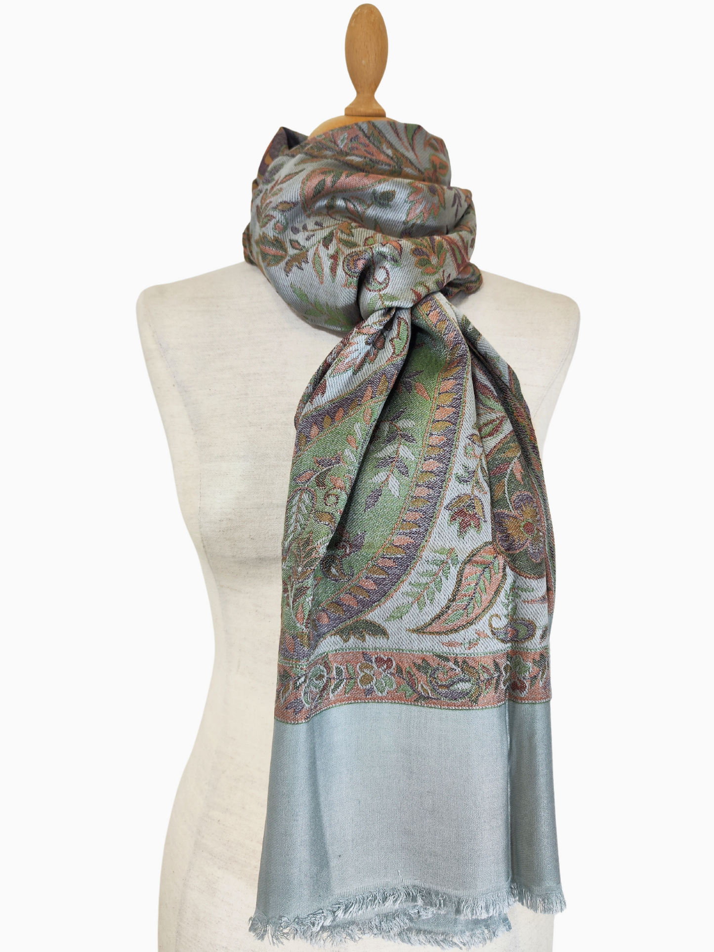 Châle en pashmina bleu clair avec un motif paisley tissé à la main dans des tons de brun, d'orange et de vert. Le châle a des bords frangés.
Un luxueux châle en pashmina avec un motif paisley classique. Le châle est drapé sur un mannequin et présente un fond bleu clair avec des détails complexes dans des couleurs chaudes.