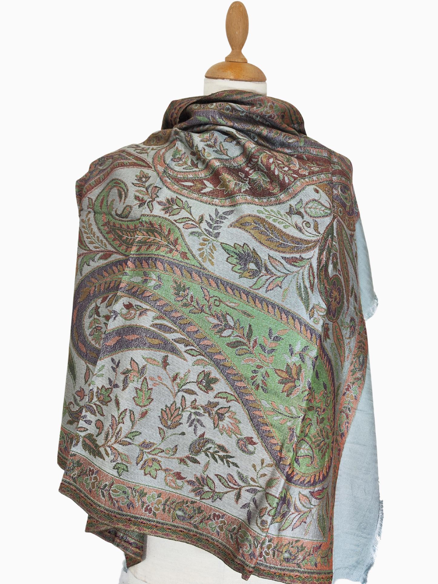 A light blue pashmina shawl with a hand-woven paisley pattern in shades of brown, orange, and green. The shawl has fringed edges.
A luxurious pashmina shawl featuring a classic paisley design. The shawl is draped over a mannequin and has a light blue background with intricate details in warm colors.