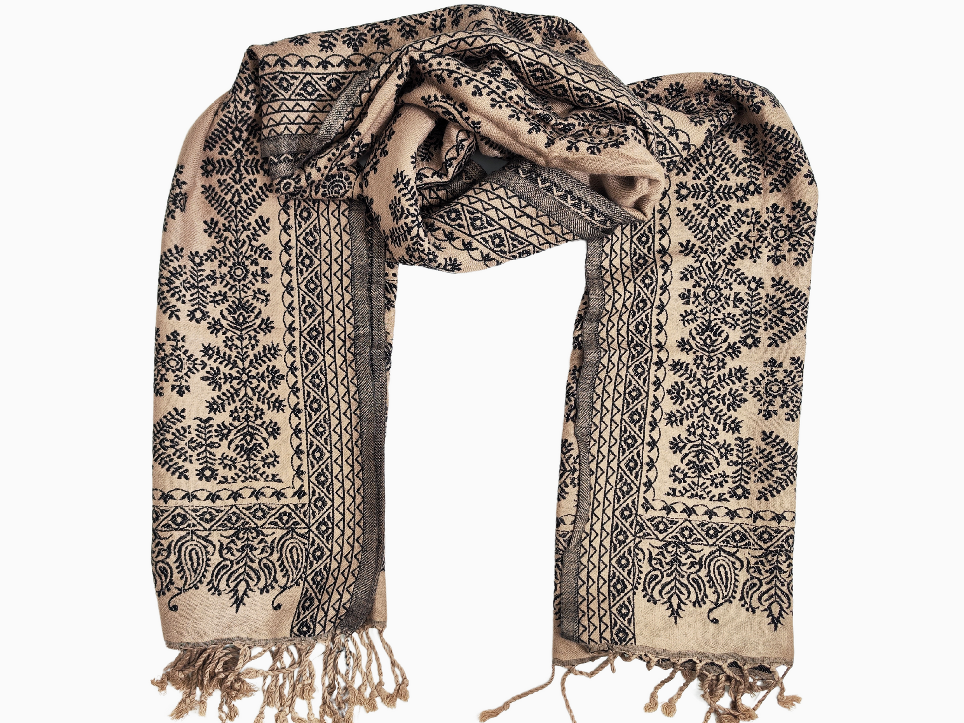 A beige shawl with intricate black floral patterns and fringed edges. A luxurious cotton-cashmere blend shawl in beige with a beautiful pattern of black floral and geometric motifs. The shawl has fringed edges.