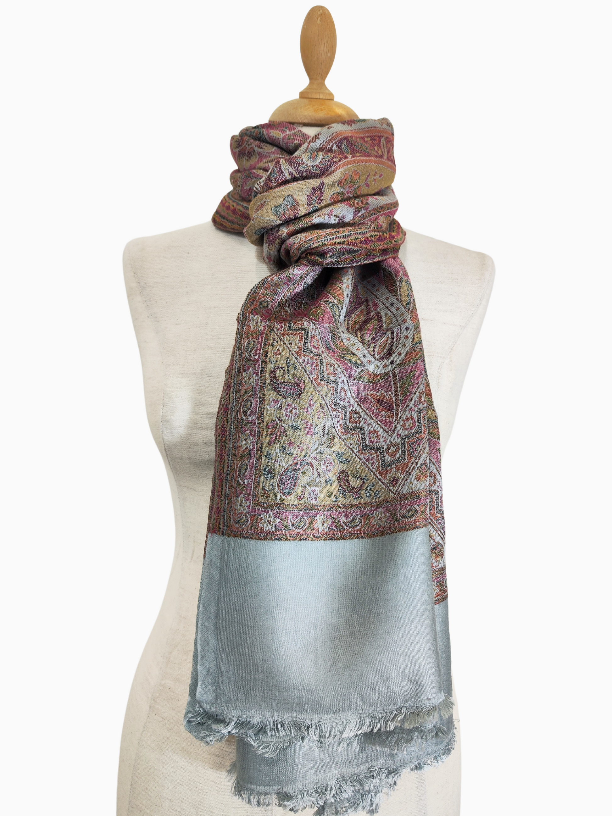 A large, rectangular scarf with a rich, intricate paisley pattern in shades of red, gold and pink on a light grey background and a grey border. It appears to be made of a soft, flowing fabric with a slight lustre.
Close-up of a fine scarf made of silk and pashmina wool with a charming paisley pattern in rich shades of red, gold and pink. scarf, warm, winter wool. silk